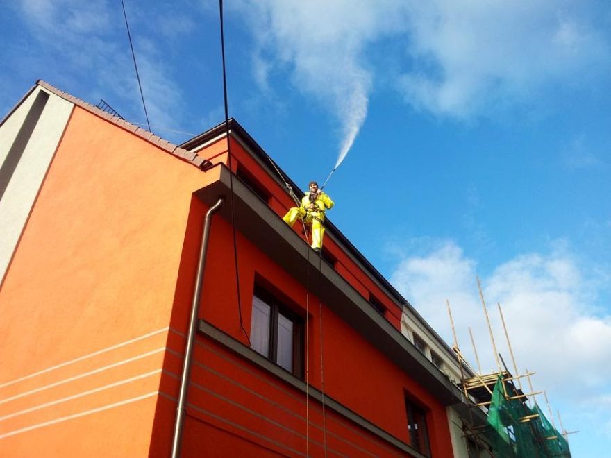 Pracovník na střeše domu při čištění fasády.